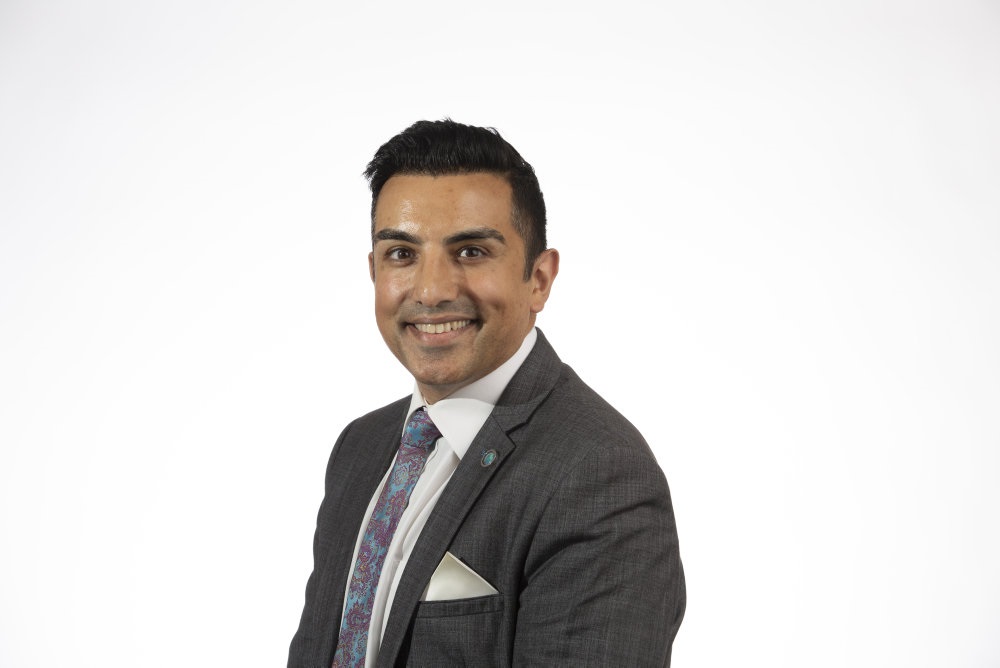 Amardeep dressed in a grey suit, smiling and looking at the camera.