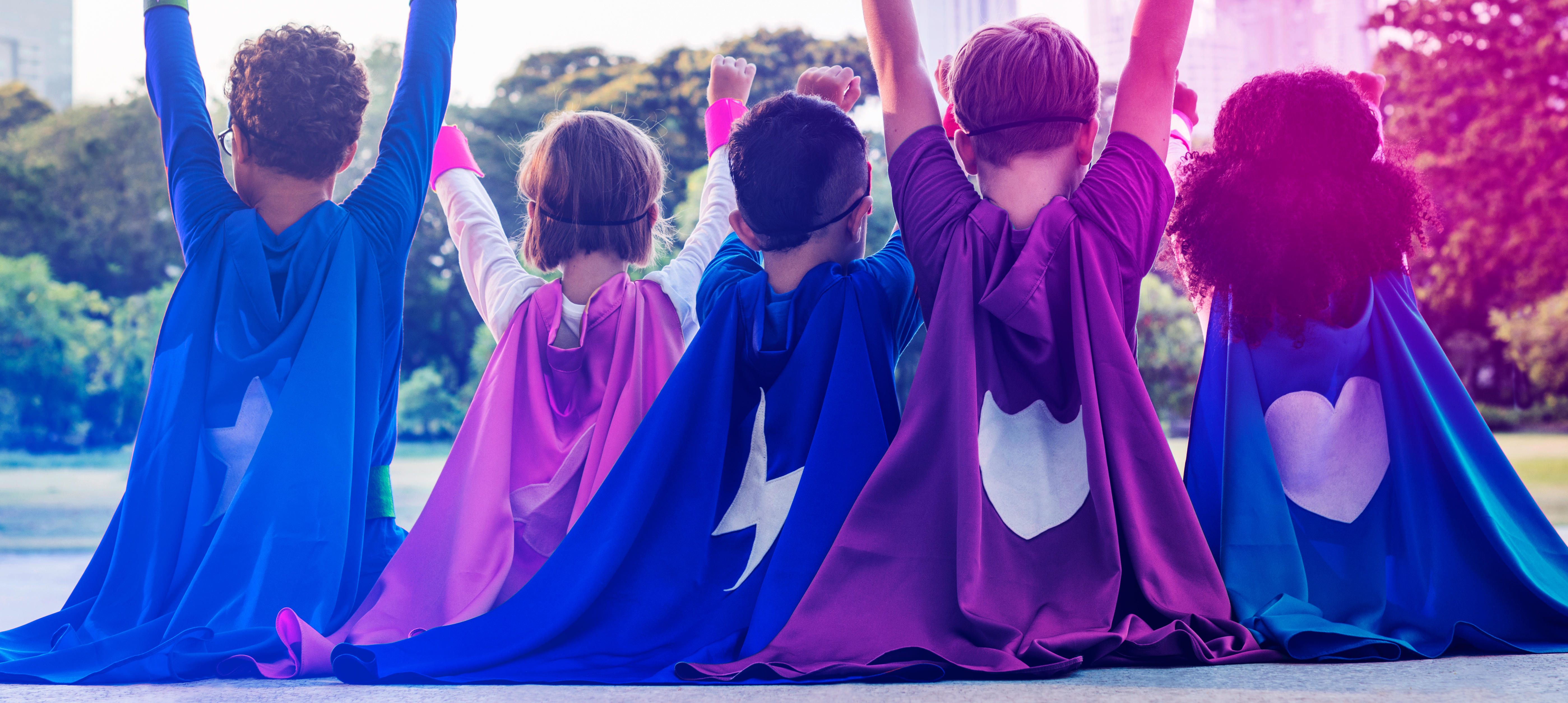 Superhero kids sit in a row facing the sunrise